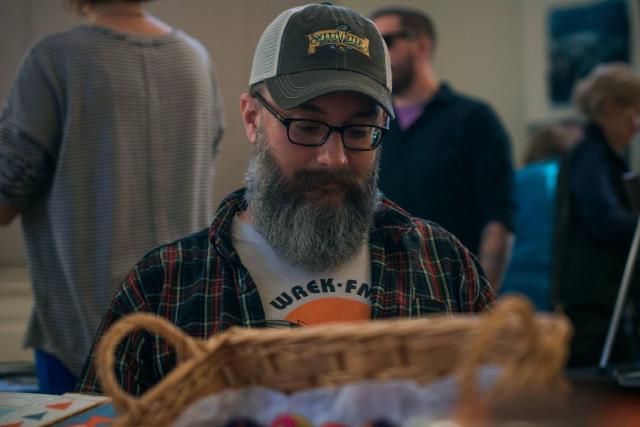 man with beard, trucker cap, and glasses looking down