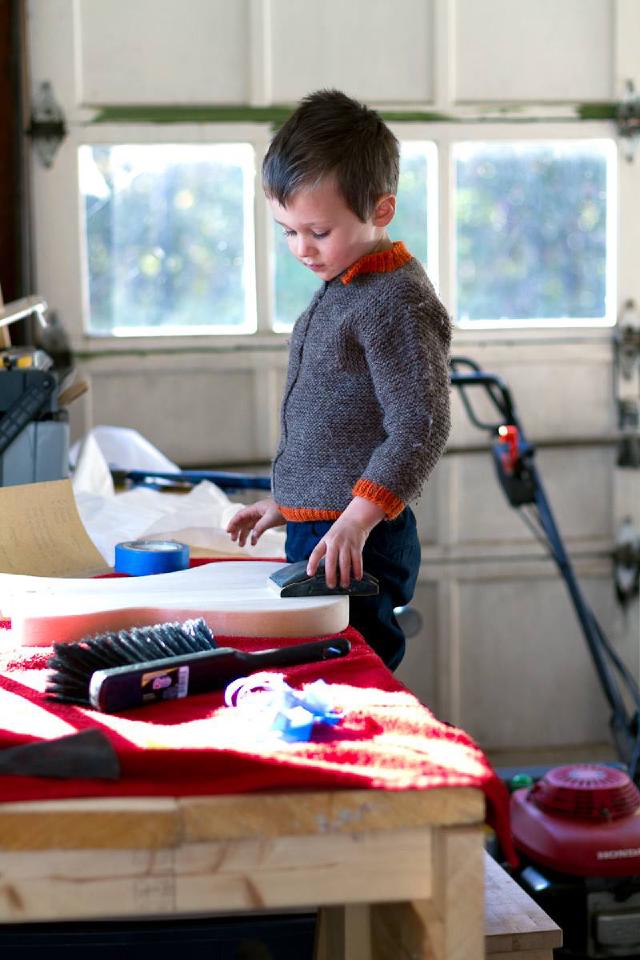 boy wearing brown sweater looks down at guitar body