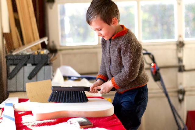 boy in brown sweater uses a large brush to dust guitar body