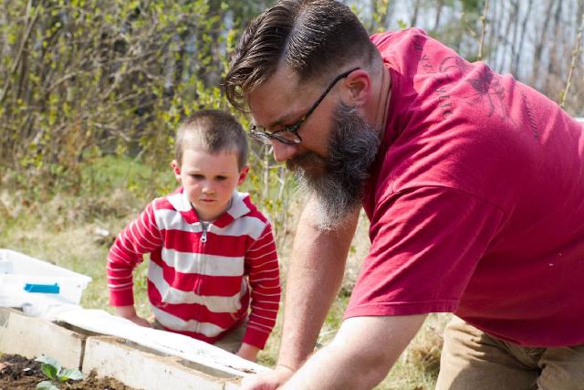 boy watches bearded man kneeling over garden