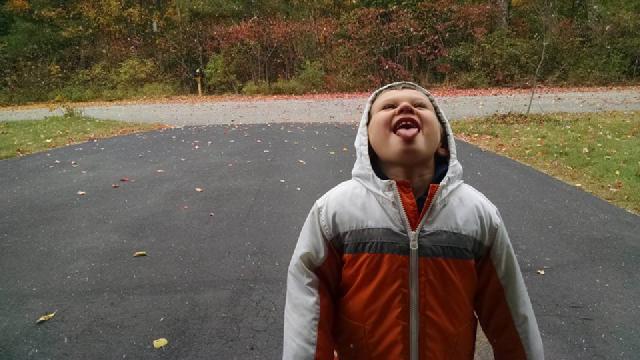 boy in white and orange jacket tries to catch snowflakes on his tongue