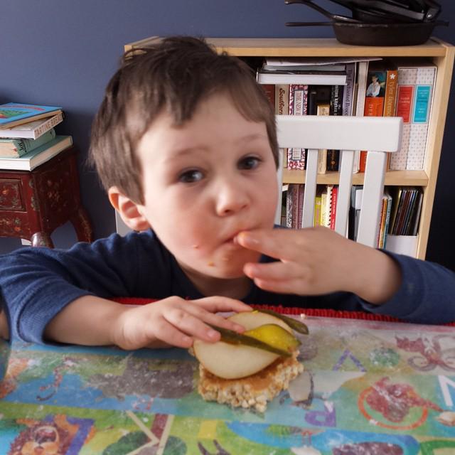 boy eating peanut butter, pears, and pickles on a rice cake