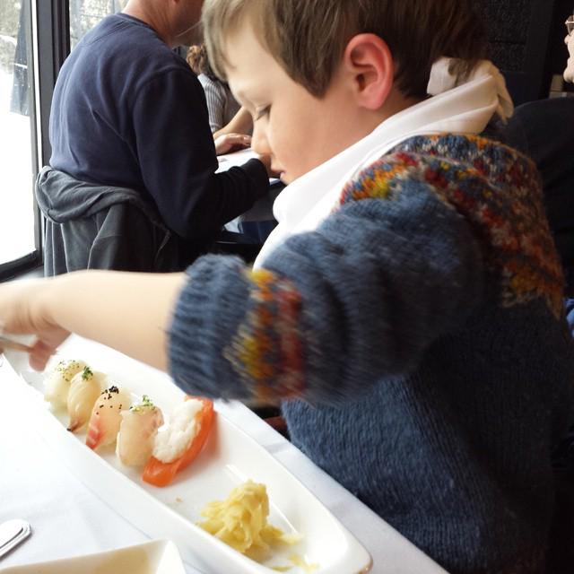 boy in a wool sweater eating a plat of sushi