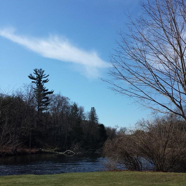 blue sky with diagonal white streak of cloud over a river and green grass