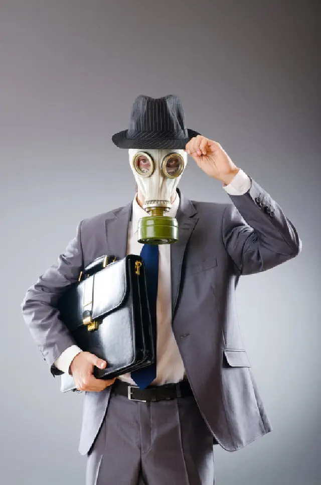 Man weaing a gas mask in gray business suit with a briefcase, tipping a black fedora