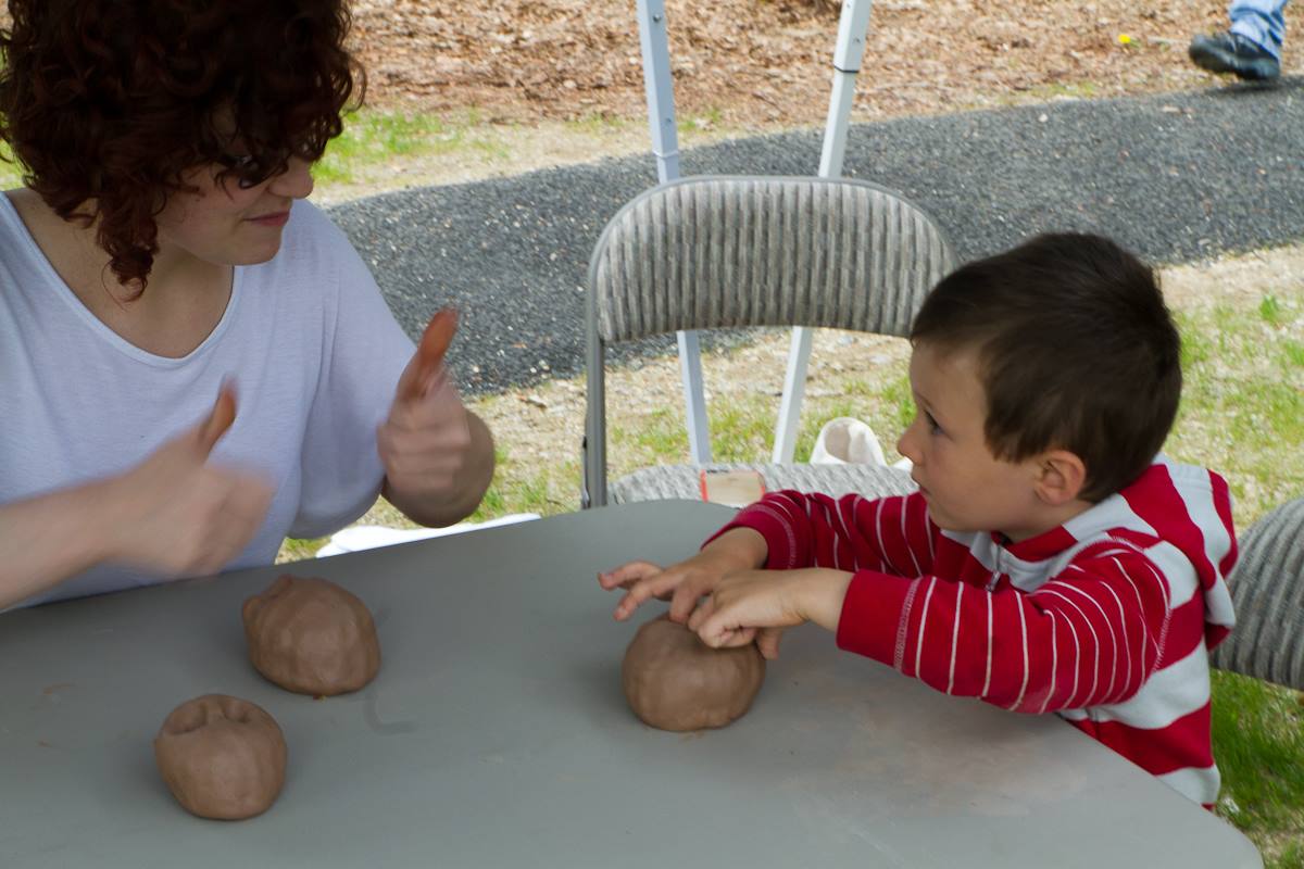 woman holding thumbs up showing boy how to form clay ball