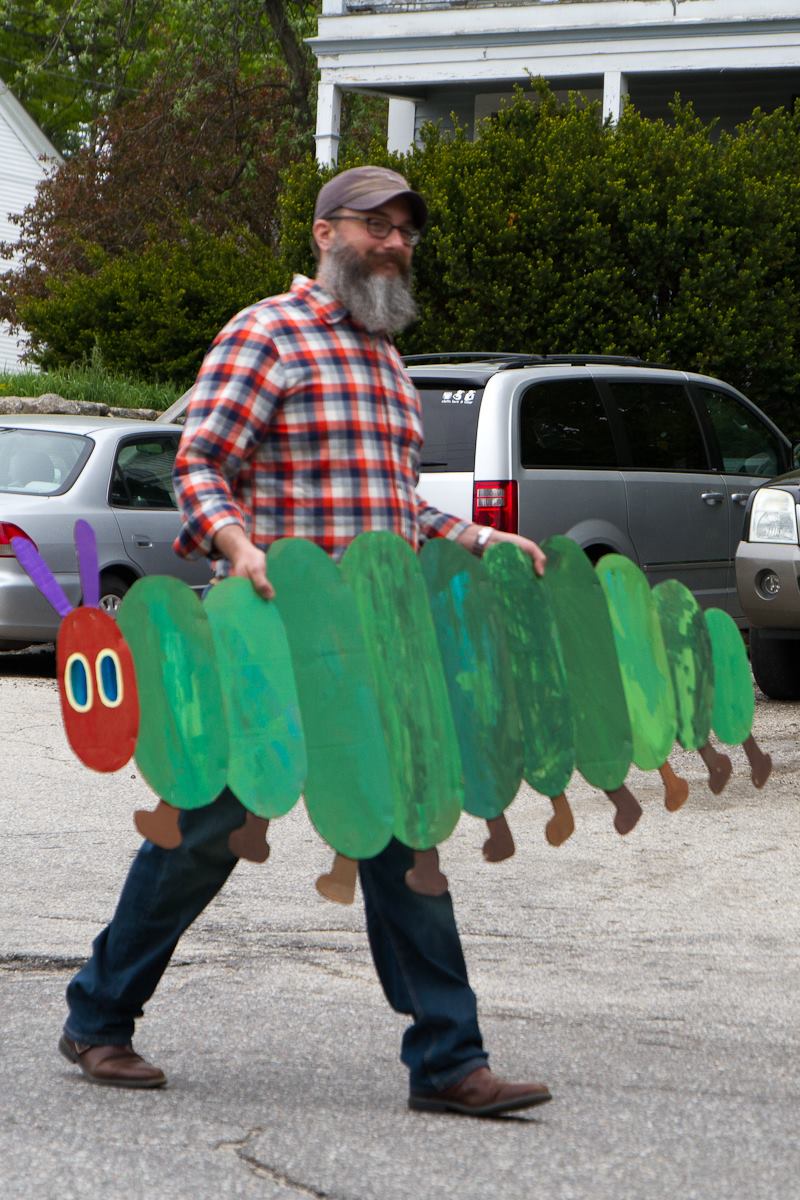man with long beard and hat carrying cardboard caterpillar