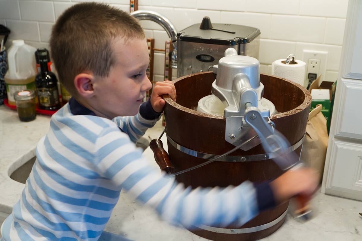 boy in light blue and white striped pajamas turning handle of ice cream churn
