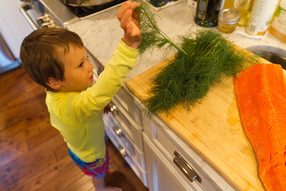 Boy in yellow shirt takes a dill frond off of kitchen counter.