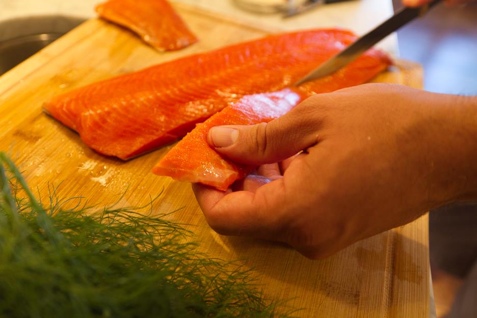 Hands and knife slicing belly off of salmon filet