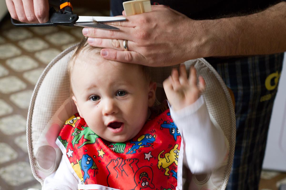 baby looking concerned while getting its hair cut by hands with scissors