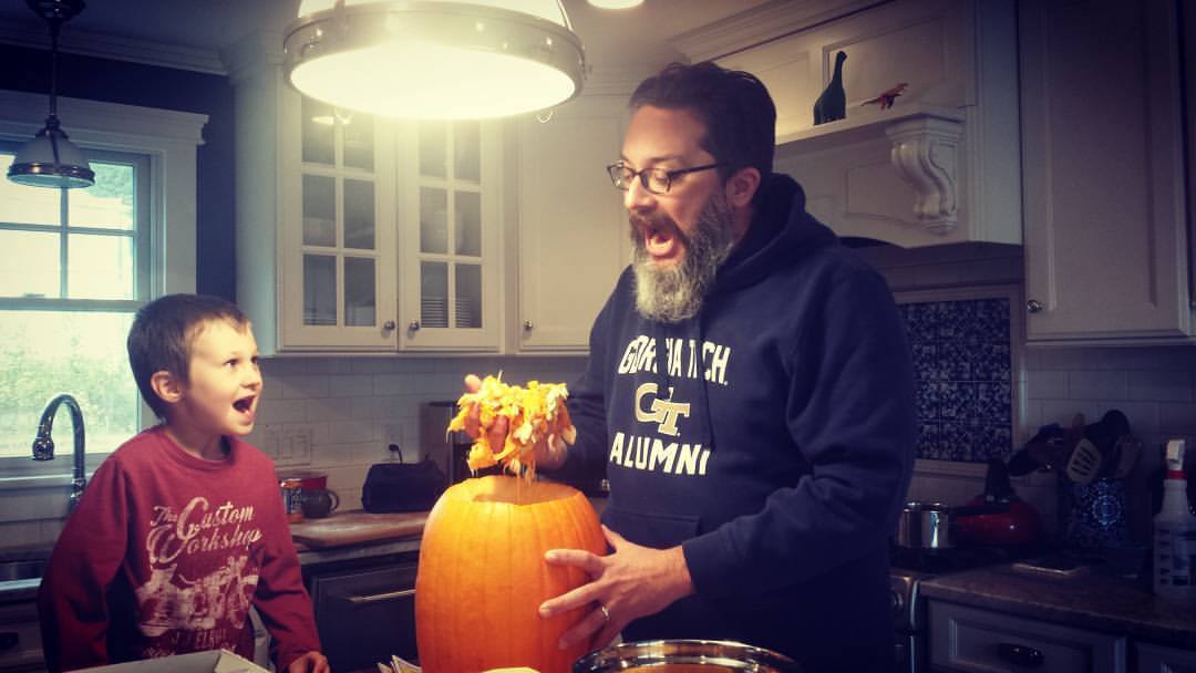 man and boy screaming while man holds a handful of pumpkin innards over a hollowed-out pumpkin