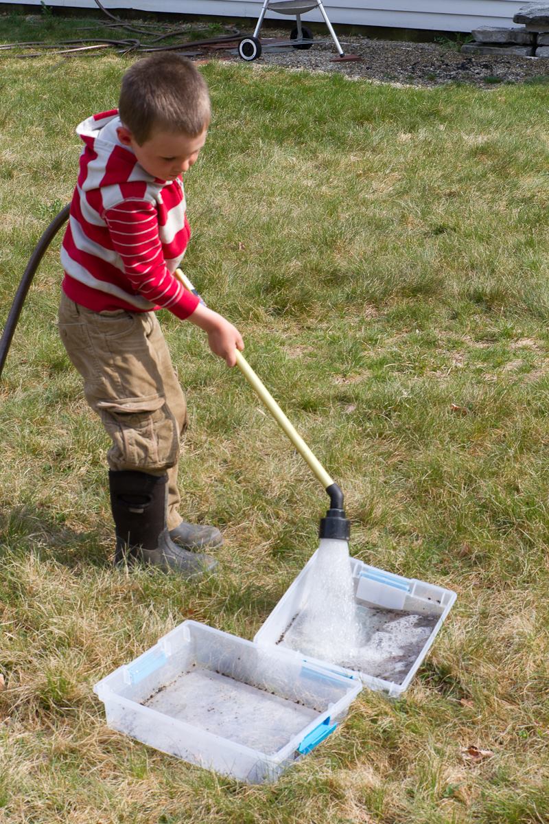 boy washes out plastic bins with spray attachment on hose
